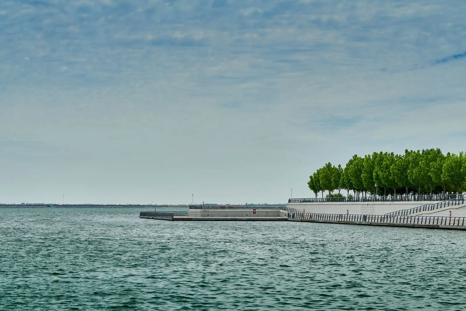 A serene view of a pier surrounded by greenery and calm waters under a clear sky.